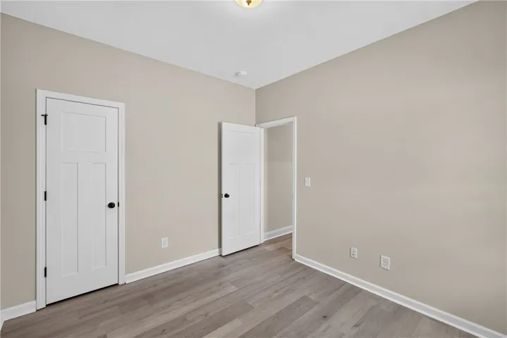 A quiet bedroom with contemporary wood-look flooring and ample wall space awaits personalization.