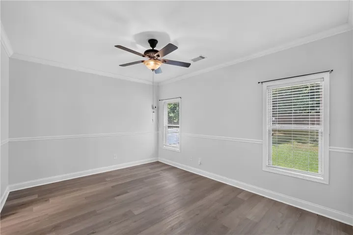 Well-lit room featuring crown molding, durable flooring, and two large windows offering verdant views.