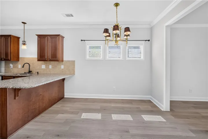 A luminous dining space features a sophisticated chandelier, sleek wood flooring, and an adjoining kitchen with granite counters.