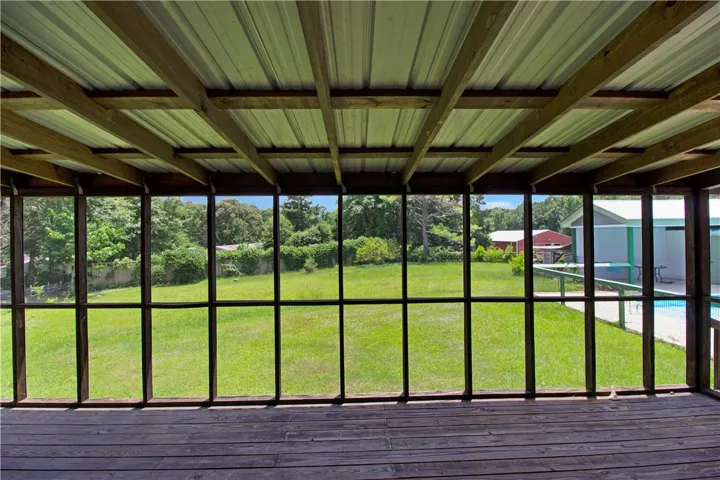 A spacious screened-in porch with wood flooring offers serene views of a verdant yard.