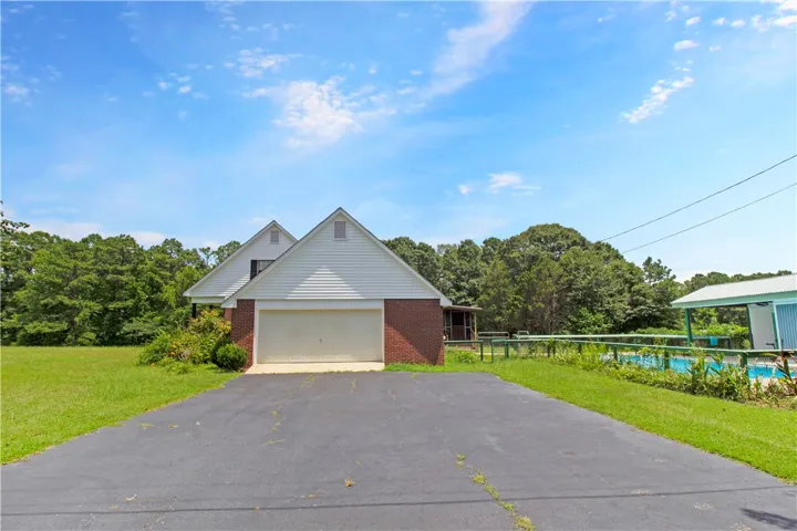 A spacious driveway leads to a charming brick home featuring an attached garage and a vibrant blue pool area.