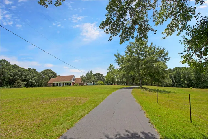 A long, inviting driveway leads to a charming residence nestled amidst a vibrant green landscape.