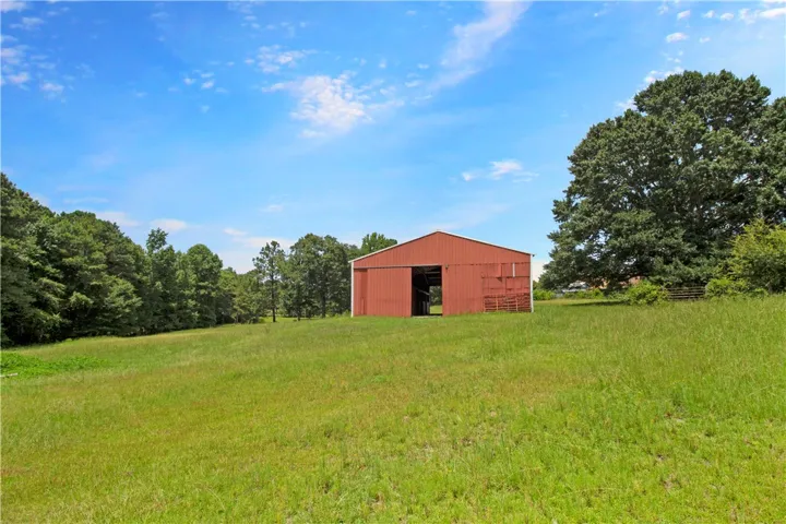 Vast green fields surround a robust red barn, nestled against a backdrop of mature trees under a clear blue sky.