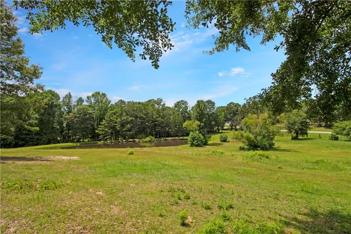 Green pastures with mature trees border a serene pond, offering an idyllic setting.