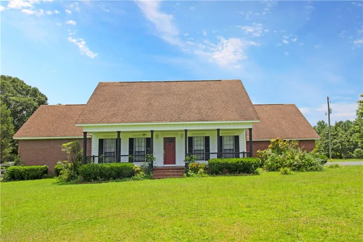 A classic ranch home, featuring a welcoming covered front porch, set on a sprawling green lawn.