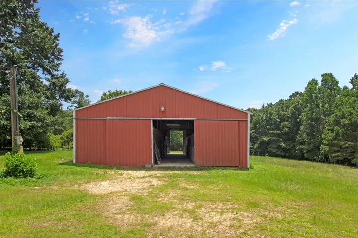 A spacious red barn with sliding doors offers versatile storage or equestrian possibilities amidst green grounds.