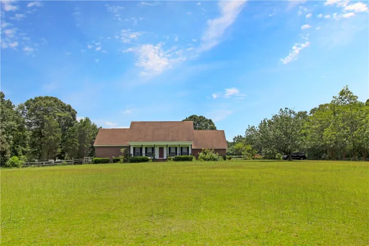 A classic brick residence set back from the road, surrounded by mature trees and vast grassy areas.