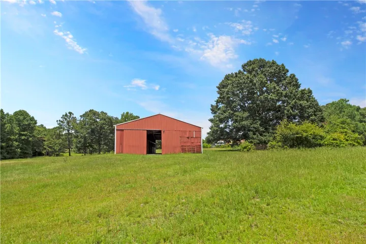 A spacious red barn sits ready for use amidst a sprawling green field under an open sky.