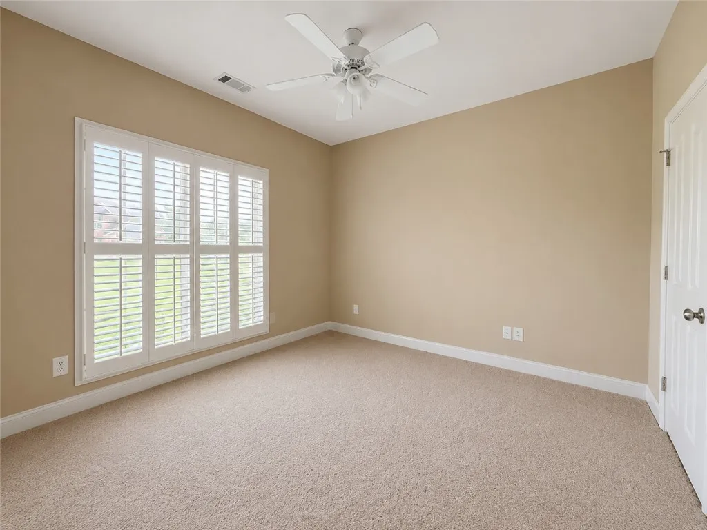 A well-lit bedroom features plush carpeting and white plantation shutters, providing both comfort and privacy.