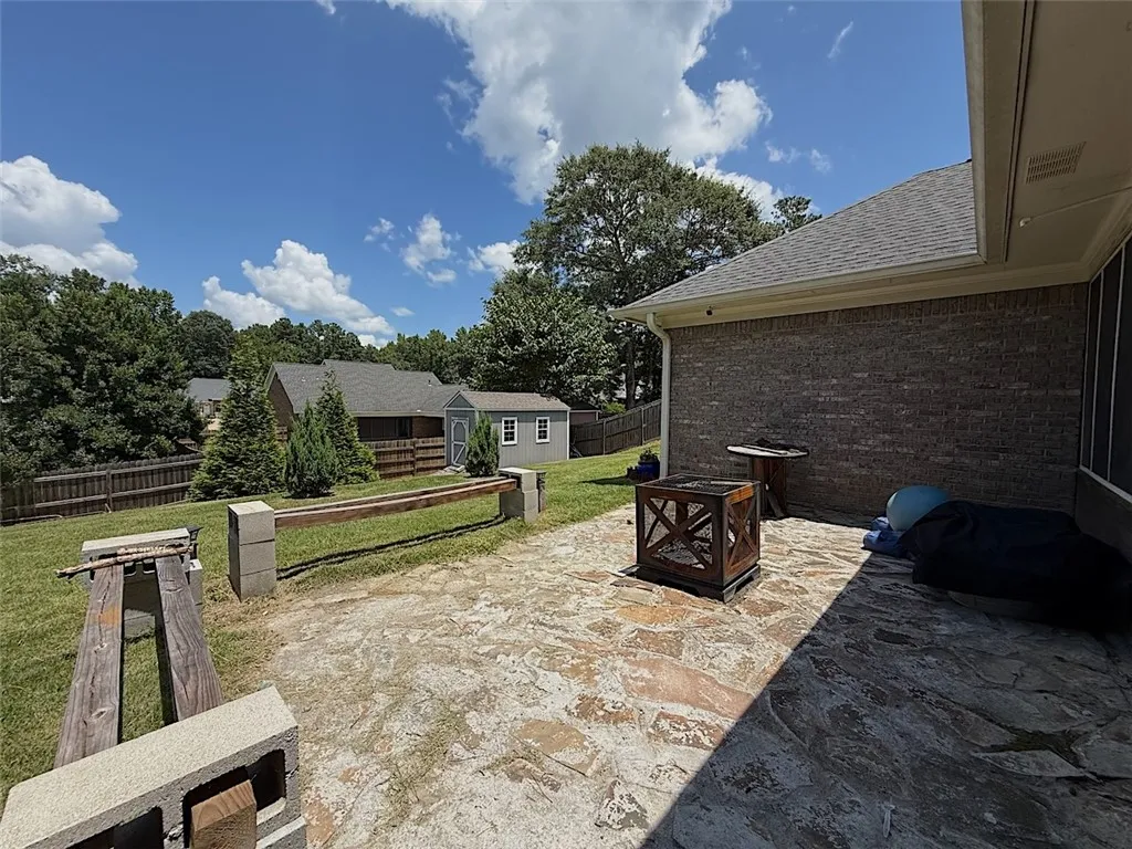 An inviting stone patio unfolds into a spacious yard with mature trees and a detached shed.