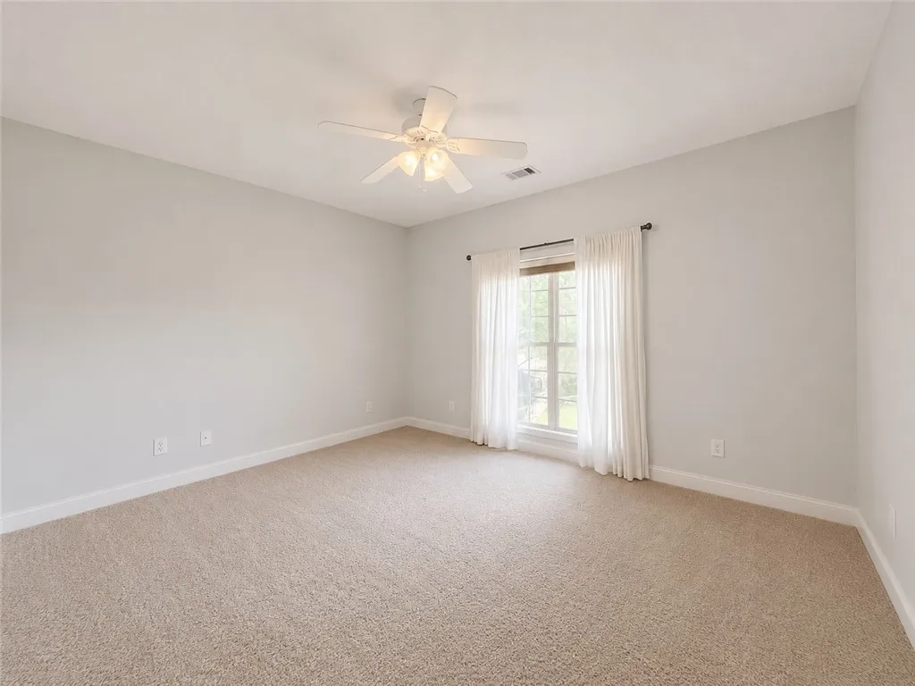 A well-lit bedroom provides a serene retreat with soft carpeting and a cooling ceiling fan.