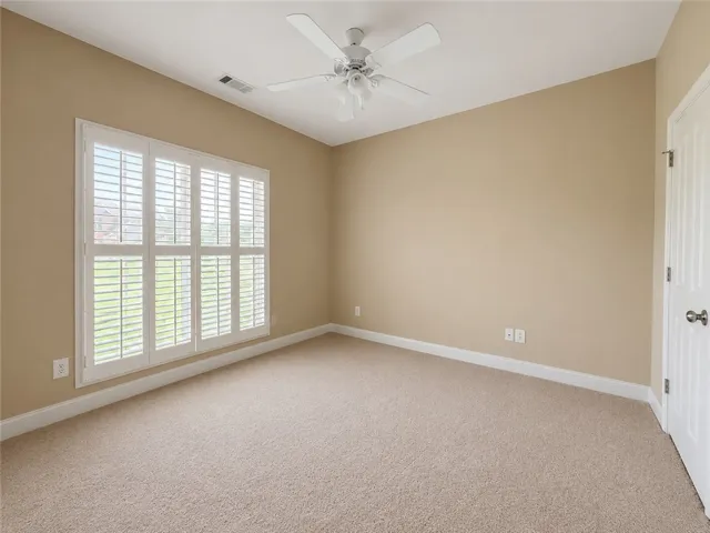 A well-lit bedroom features plush carpeting and white plantation shutters, providing both comfort and privacy.