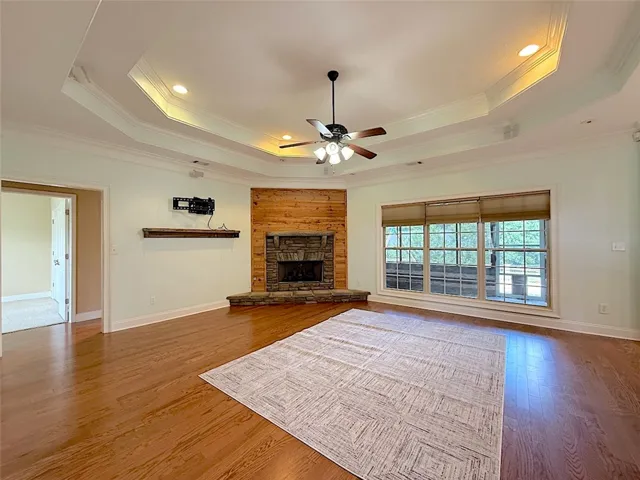 A spacious living area features rich hardwood flooring and a charming stone fireplace with a rustic wood mantle.