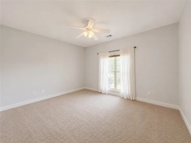 A well-lit bedroom provides a serene retreat with soft carpeting and a cooling ceiling fan.