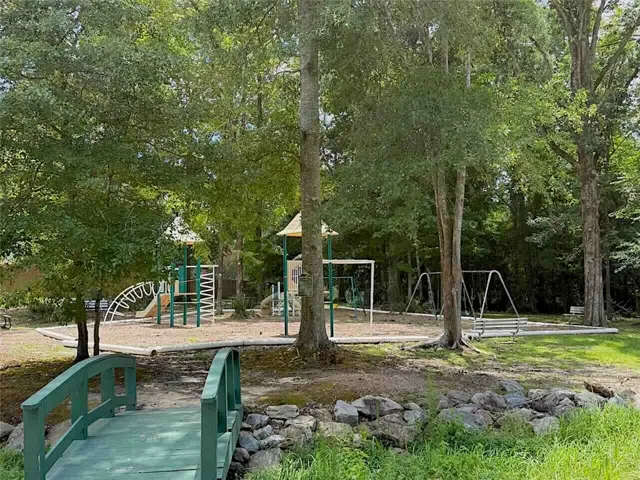 A charming wooden bridge leads to a shaded playground area, perfect for community recreation.