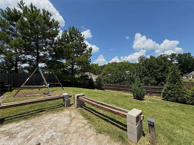 A spacious, naturally illuminated yard offers ample room for recreation and privacy, bordered by mature trees and a wooden fence.