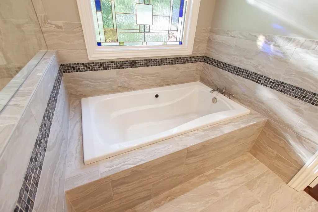 Indulge in a tranquil soak within this well-appointed bath featuring elegant tile work and a charming stained-glass window.
