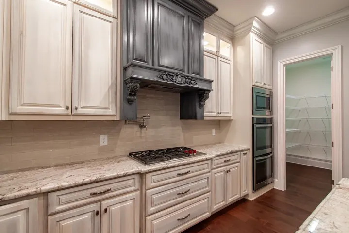 A well-appointed kitchen showcasing a Wolf gas range, pot filler, double oven, and granite countertops, with a convenient pantry just steps away.
