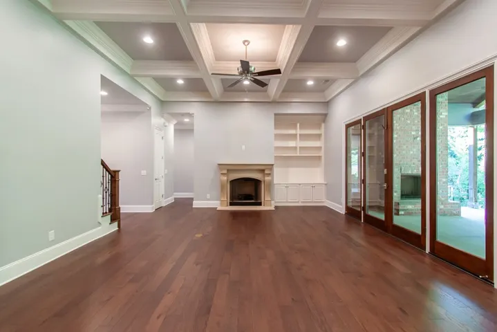 Hardwood flooring extends throughout this expansive living area, complemented by coffered ceilings, a stately fireplace and built-in shelving.