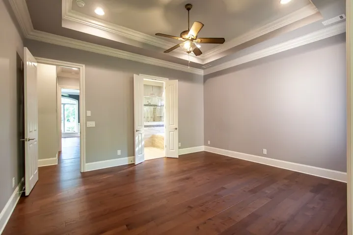 Elegant hardwood flooring grounds this naturally illuminated bedroom with a striking tray ceiling and ceiling fan.