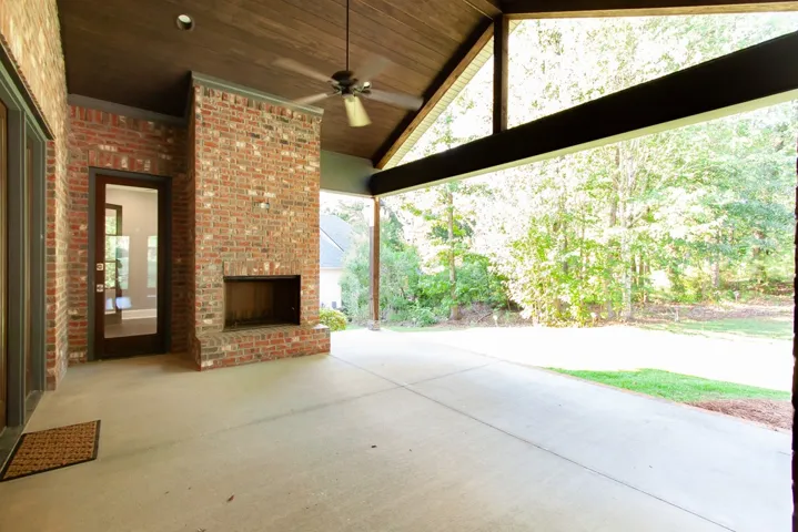 An inviting covered patio featuring a brick fireplace and a vaulted wood-paneled ceiling with a fan, perfect for enjoying the serene wooded backyard.