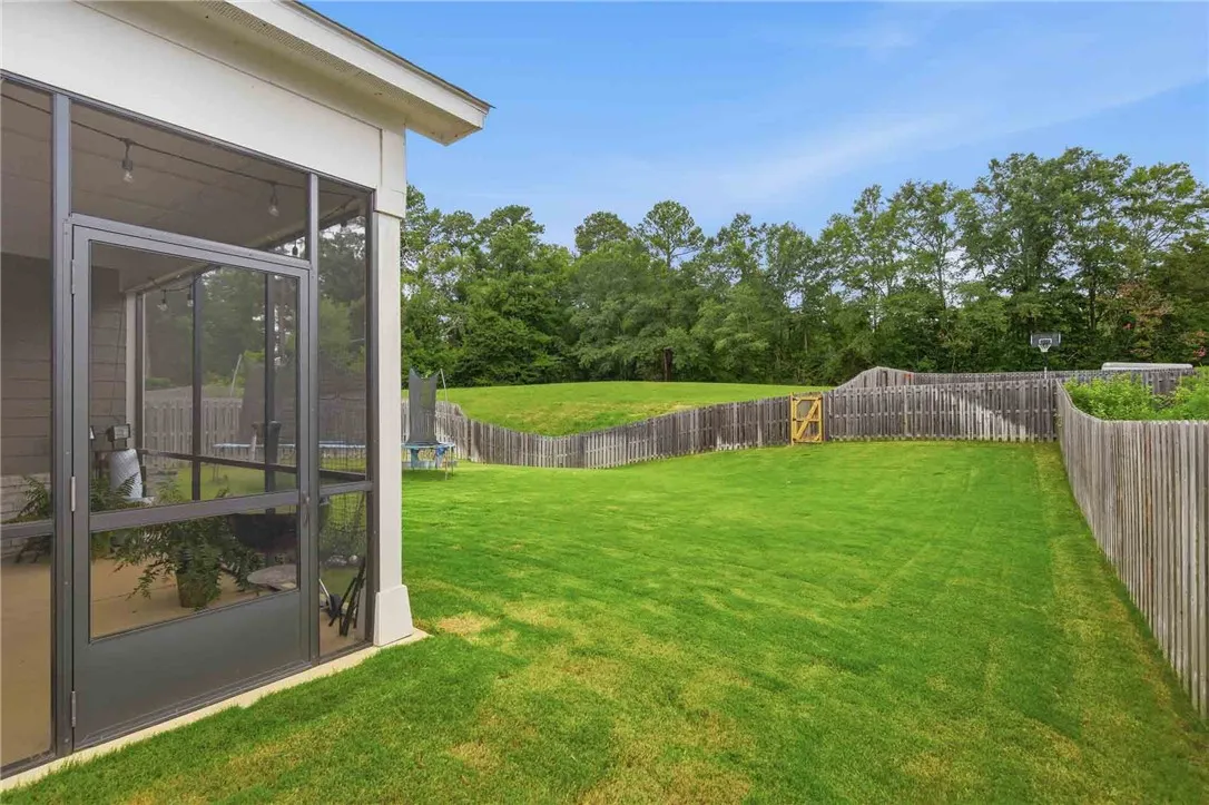 A spacious, verdant lawn extends from a screened patio to a privacy fence bordering a natural treeline.