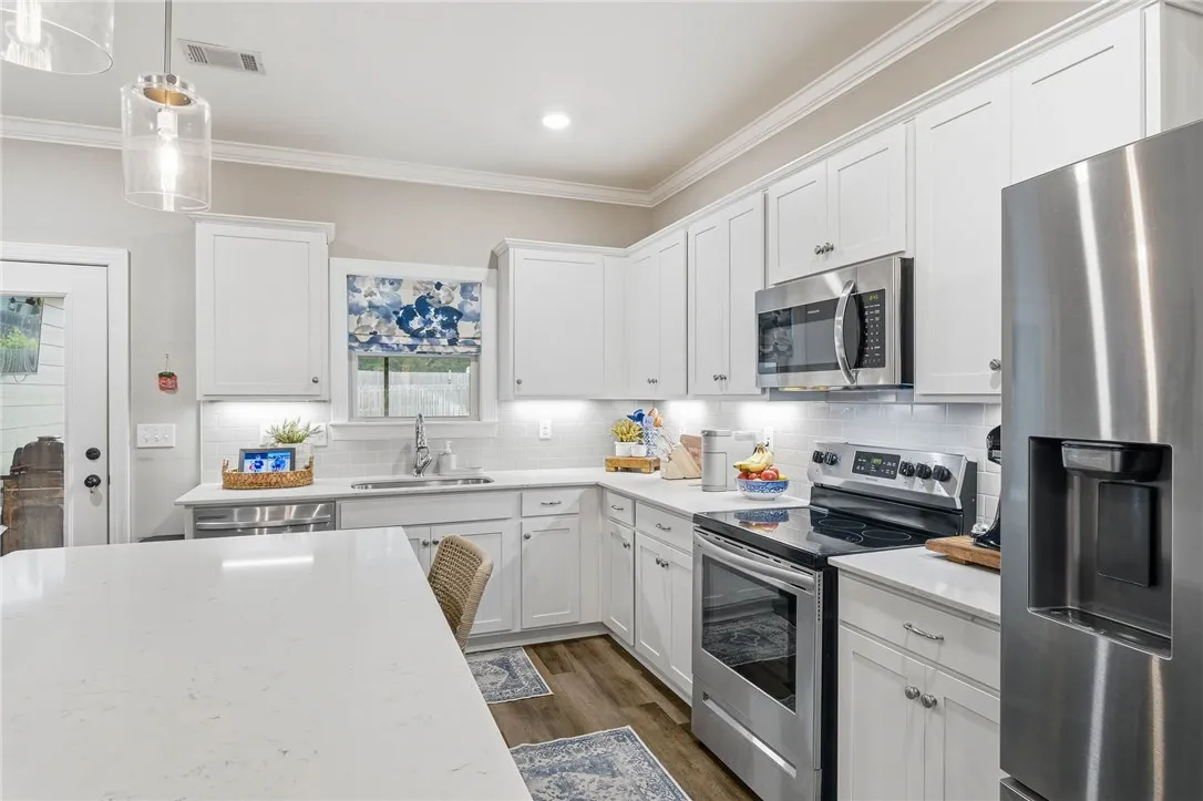A pristine culinary space boasts white cabinetry, modern stainless-steel appliances, and resilient hardwood flooring.