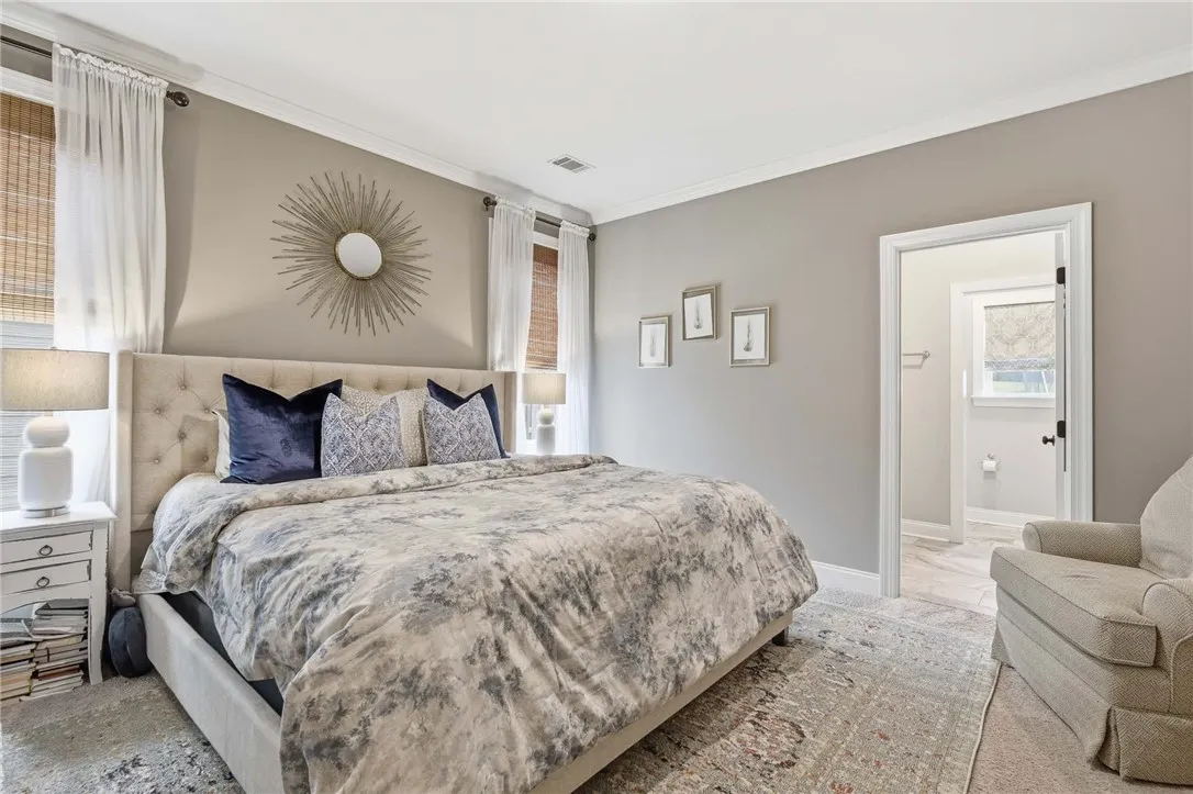 A well-lit bedroom features crown molding and a doorway leading to an adjacent bathroom.