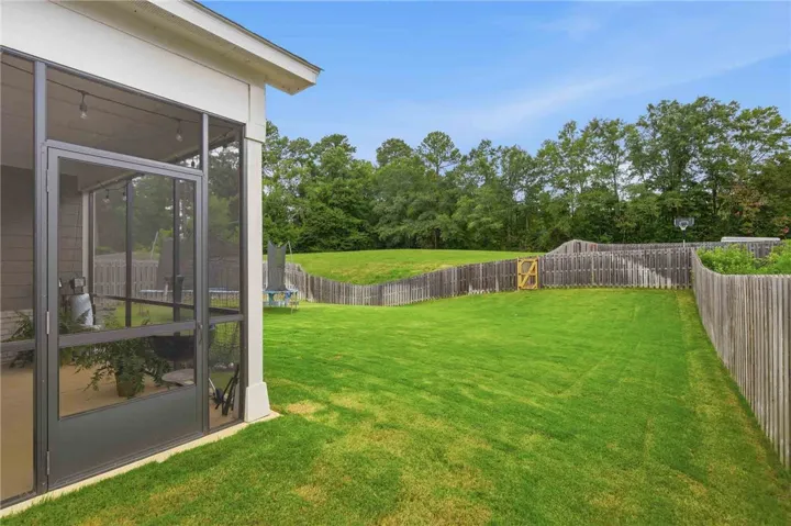 A spacious, verdant lawn extends from a screened patio to a privacy fence bordering a natural treeline.
