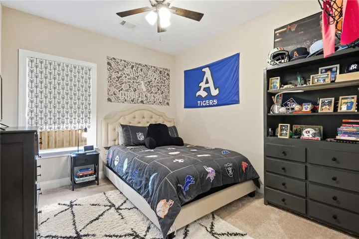 A well-lit bedroom features a comfortable bed, a bookshelf, and a ceiling fan for optimal comfort.