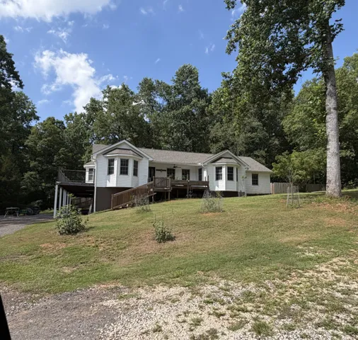 Perched on a grassy hill, this home offers expansive outdoor living with multiple decks surrounded by mature trees.