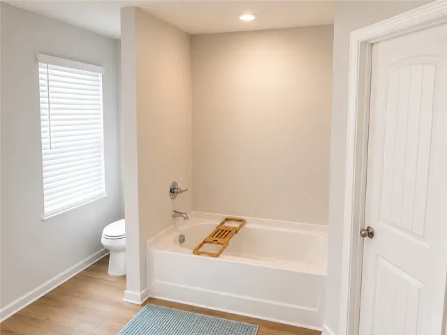 A well-appointed bathroom with a clean, contemporary design features a spacious tub and warm wood flooring.
