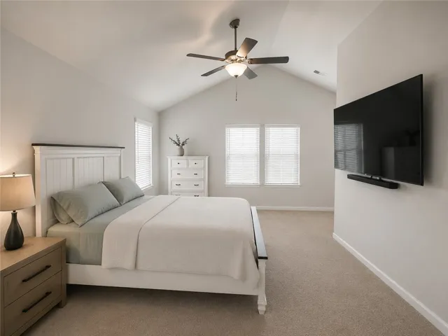 The generously proportioned bedroom presents high vaulted ceilings and a soothing neutral color palette.