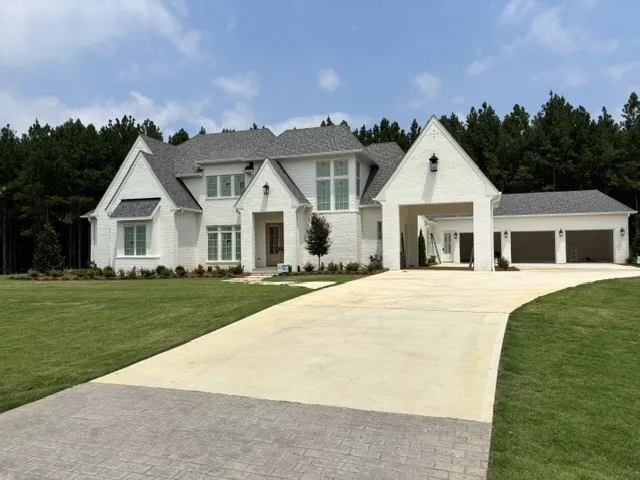 A grand white brick residence awaits, boasting a prominent driveway and a spacious three-car garage.
