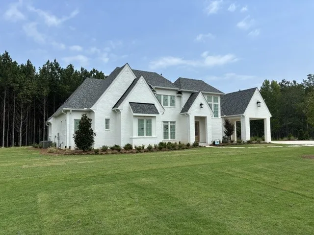 A distinguished white brick home with a gray shingle roof sits gracefully amidst a verdant lawn.