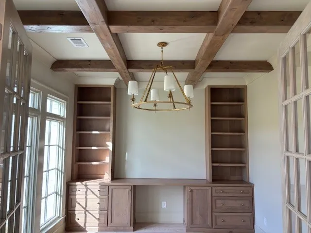 Crafted wooden built-ins flank a spacious workspace beneath a striking coffered ceiling.