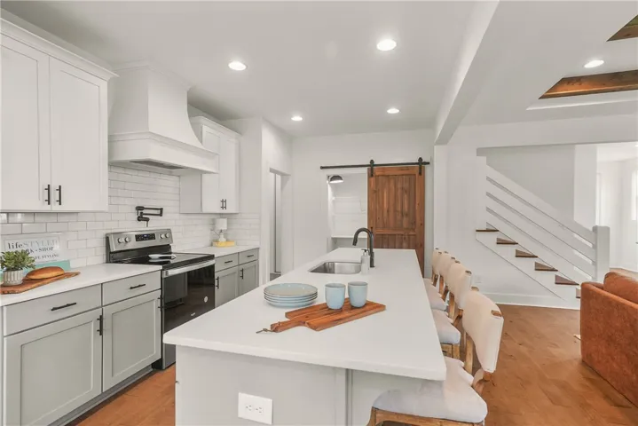 Kitchen features a large center island, farm sink, quartz countertops and wood hood
