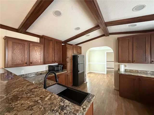 Rich wood beams trim the vaulted ceiling above solid stone counters and matching cabinetry.