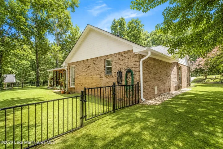 A well-maintained brick exterior nestles into a verdant landscape, secured by a sleek iron fence.