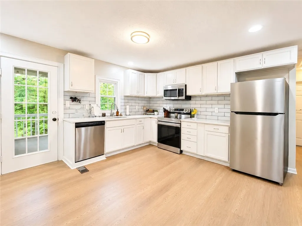 A well-appointed kitchen features ample white cabinetry, gleaming stainless steel appliances, and durable hardwood flooring.