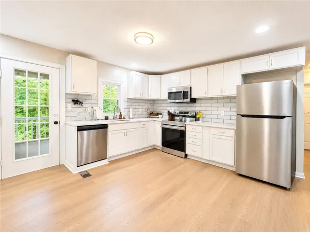 A well-appointed kitchen features ample white cabinetry, gleaming stainless steel appliances, and durable hardwood flooring.