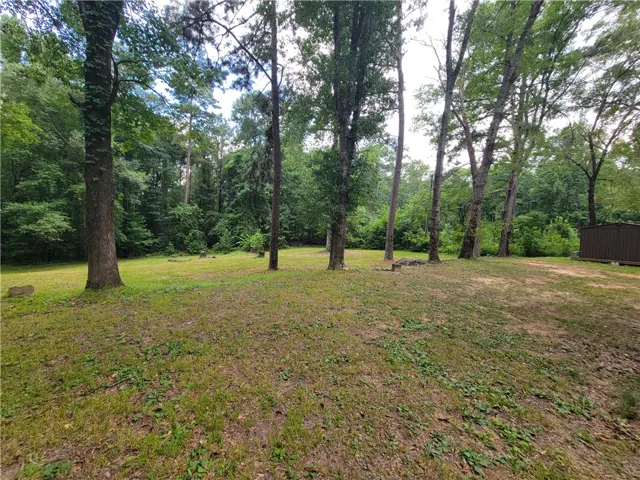 A spacious green lawn is framed by towering trees and a secluded storage shed, perfect for outdoor living.
