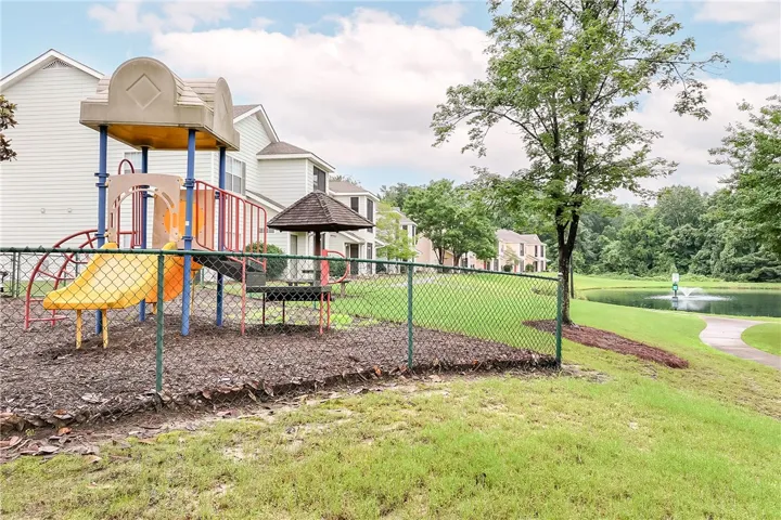 A well-maintained playground awaits  residents, adjacent to a pond and walking path.