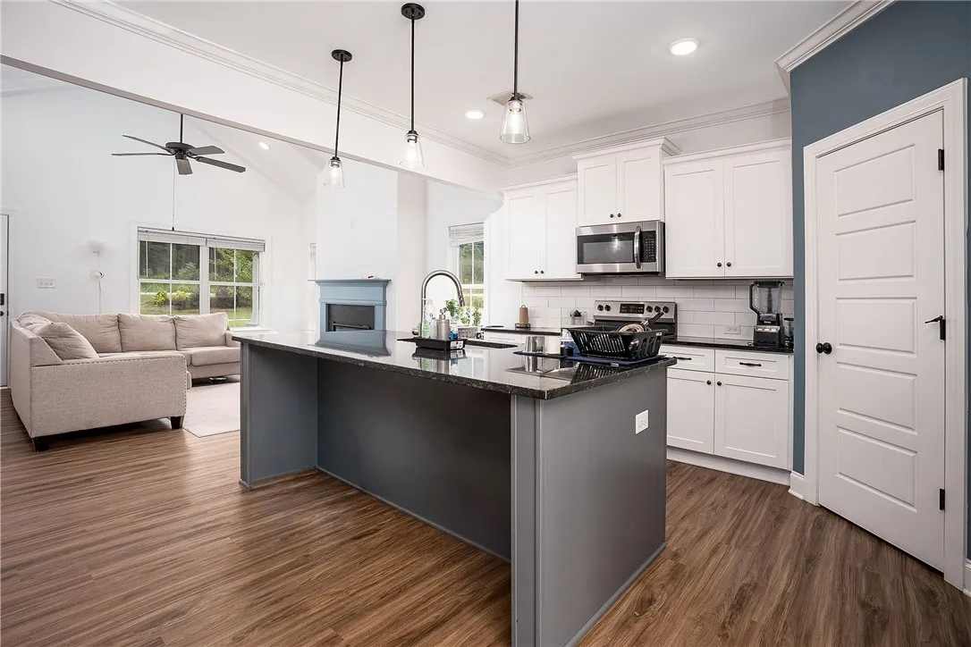 An open-concept living space presents a kitchen island with pendant lighting and views into a relaxed sitting area with a fireplace.