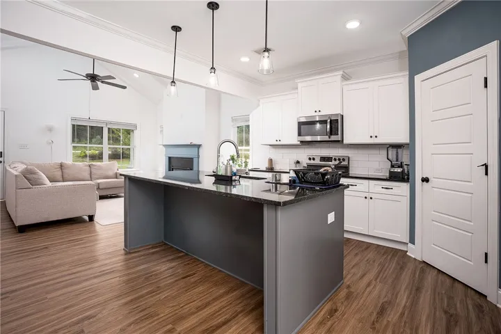 An open-concept living space presents a kitchen island with pendant lighting and views into a relaxed sitting area with a fireplace.