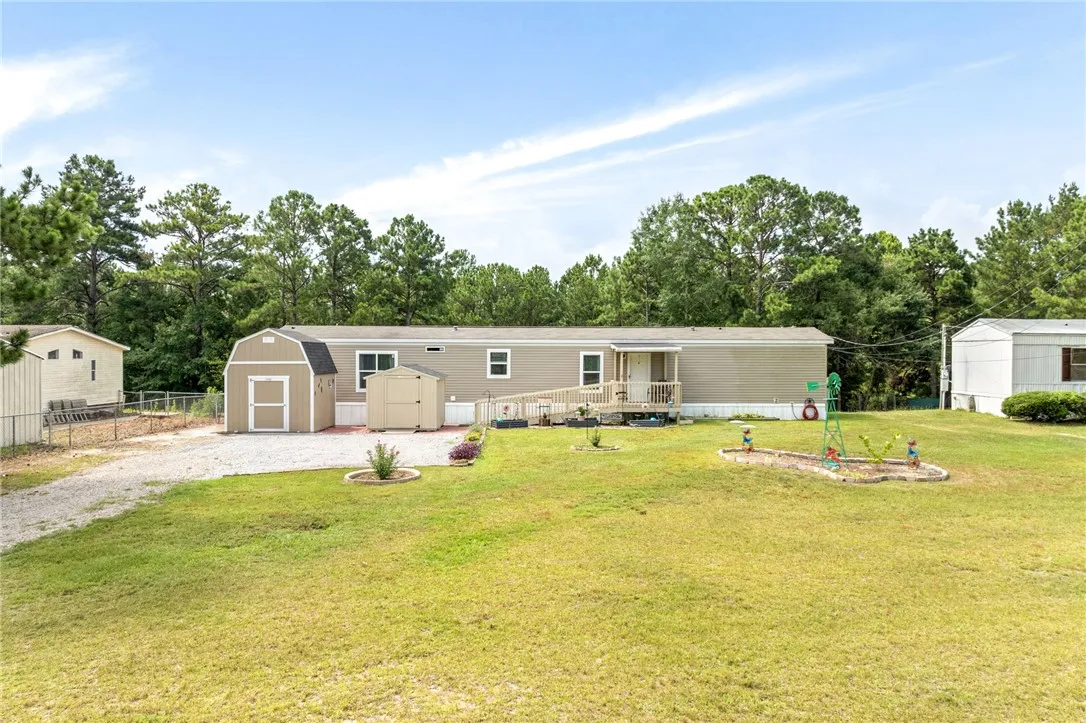 A generous grassy lot hosts a well-maintained manufactured home, complete with multiple storage sheds and a welcoming front porch.