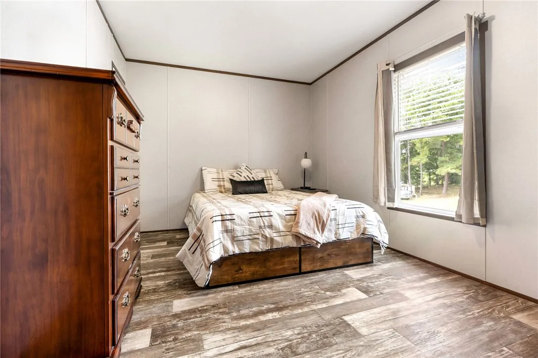 Gleaming wood-look floors anchor this bedroom featuring a large window looking out to the trees.