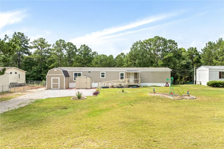 A generous grassy lot hosts a well-maintained manufactured home, complete with multiple storage sheds and a welcoming front porch.