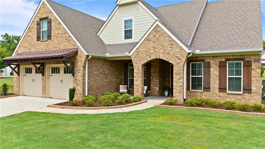A classic brick exterior with a welcoming arched entry and double garage doors, set against a manicured lawn.