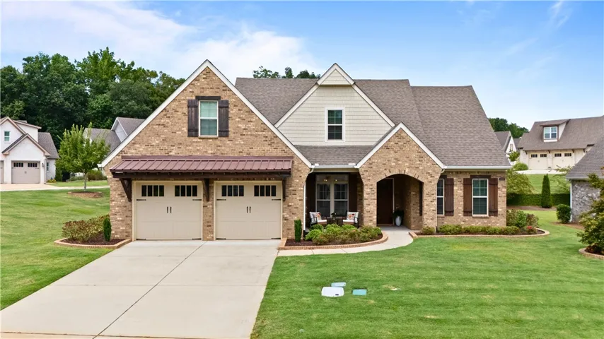 A welcoming brick-clad residence with a double garage, lush green lawn, and a charming covered front porch.